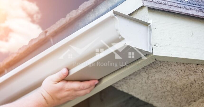 Hands installing a white rain gutter on a house eave in bright sunlight