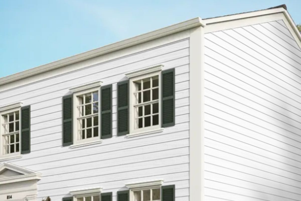 White colonial house with green shutters and multi-pane windows against blue sky