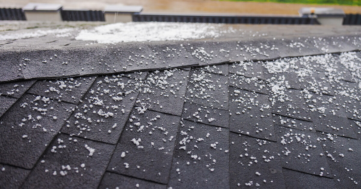 Close-up of a roof with small hailstones scattered across dark shingles.