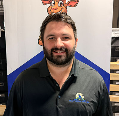 Smiling man in black polo shirt with animal logo, standing indoors.