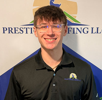 Smiling person in branded black shirt at Prestige Roofing LLC backdrop.