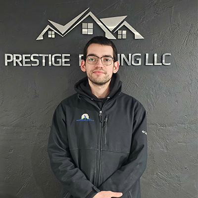 Man standing in front of Prestige Roofing LLC sign on a textured wall.
